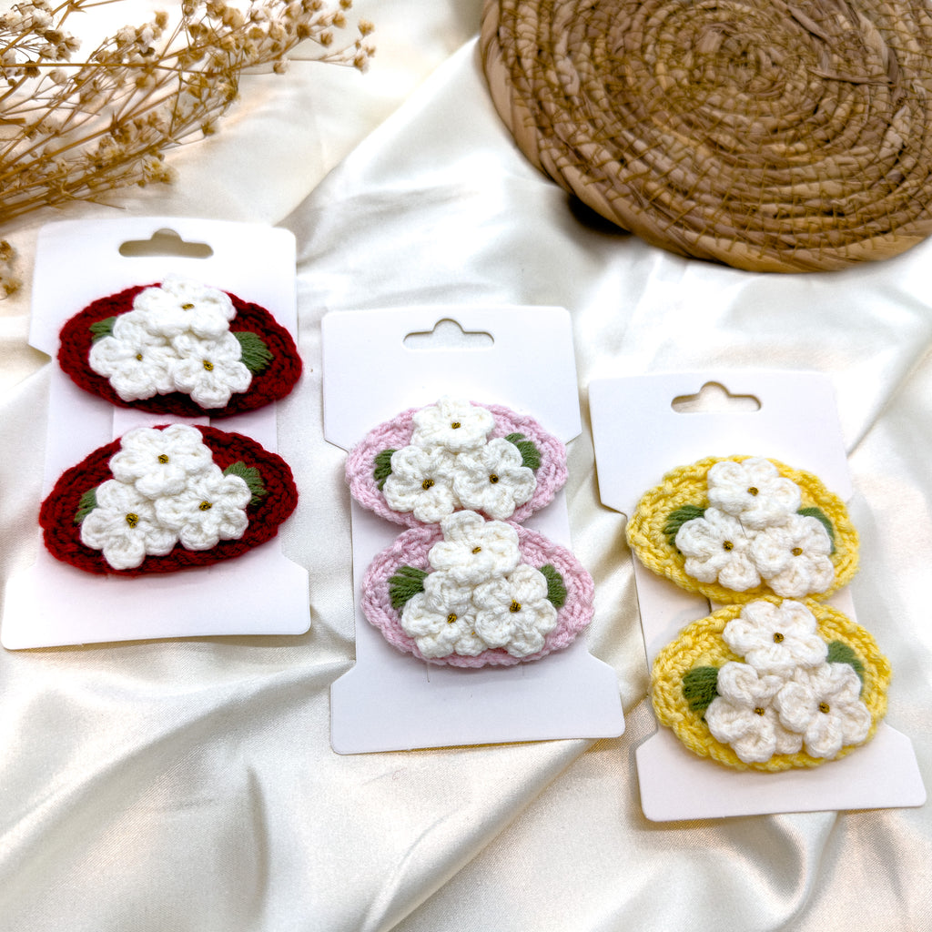 Set von handgefertigten Blumen-Haarspangen in den Farben Rot, Hellrosa und Gelb, verziert mit gehäkelten Blumen auf weißem Hintergrund.
