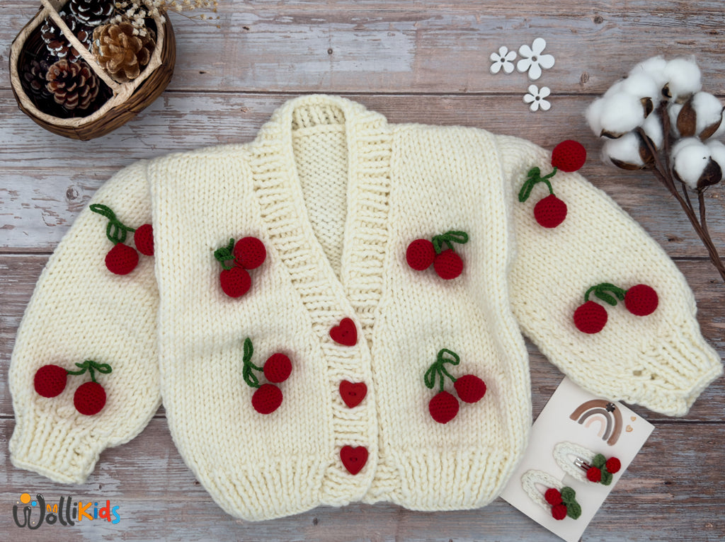 Handgestrickte Kirschzeit-Strickjacke-in-Creme mit Kirschenmotiven und Herzchenknöpfen, aus 75 % Polyacryl und 25 % Schurwolle – warm und komfortabel.