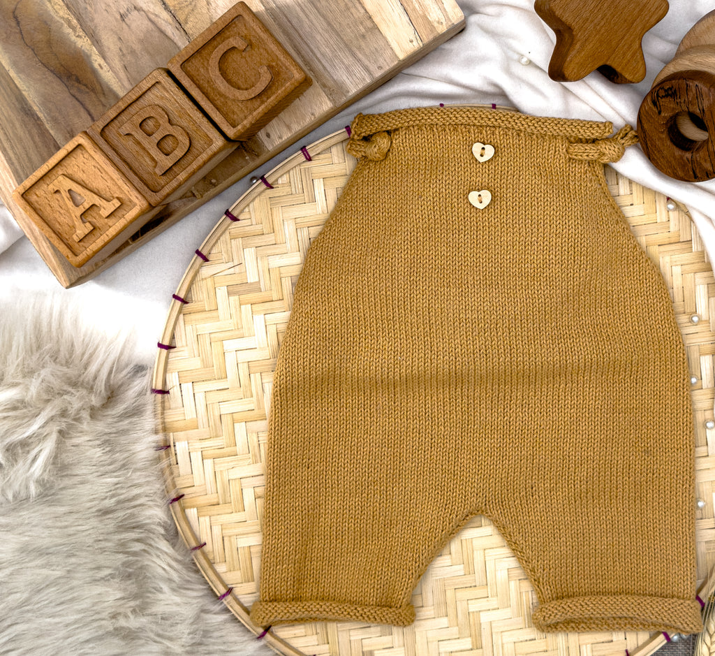 Vintage-Handgestrickter-Neugeborenen-Strampler in Safran, elegant präsentiert auf einem dekorativen Bambuskorb mit Holzspielzeug.